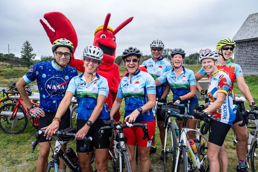 A picture of 7 cyclists with the Lobster mascot at a rest stop during the Gran Fondo Baie Sainte-Marie.